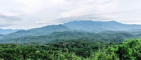 A wooden deck overlooking a mountainous landscape with dense greenery and a clear sky.