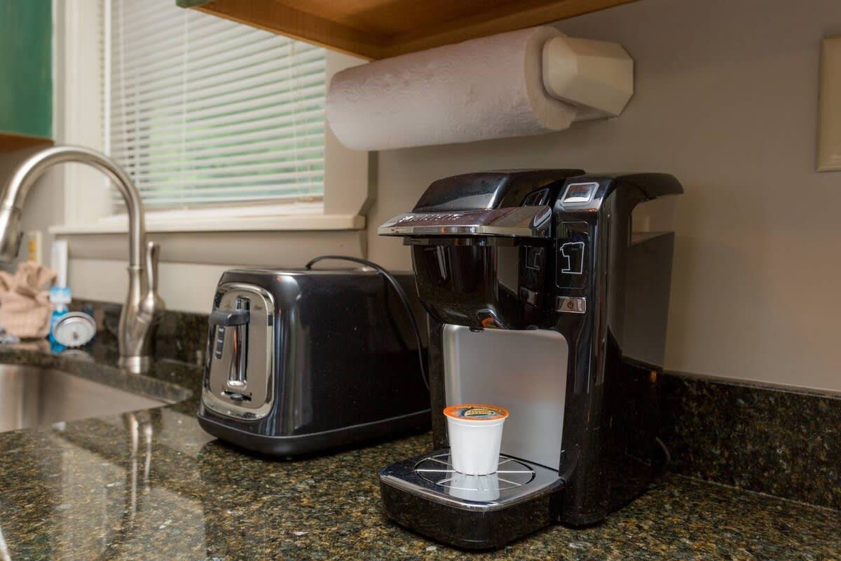 Een koffiezetapparaat met bekerhouder, een broodrooster en een papieren handdoekdispenser op een keukenaanrecht.