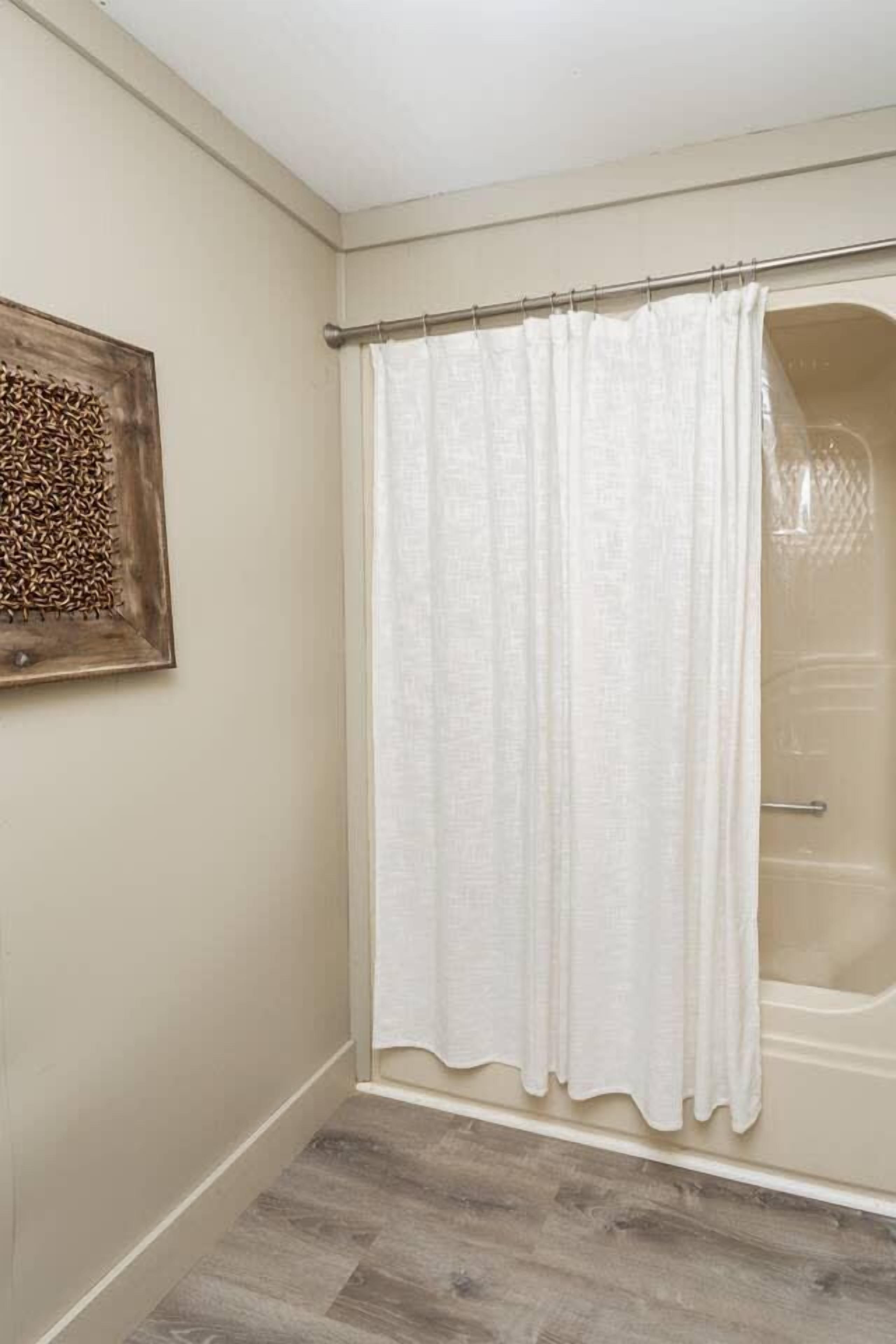 Une salle de bain avec un rideau de douche, une œuvre d’art en bois accrochée au mur et un sol carrelé.