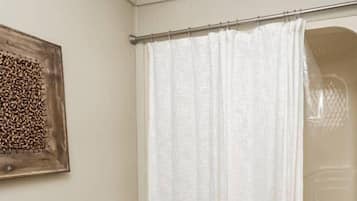 Une salle de bain avec un rideau de douche, une œuvre d’art en bois accrochée au mur et un sol carrelé.