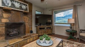 A living room with a stone fireplace, a television, and a view of mountains through a window.