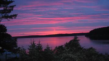 Rauhallinen näkymä järvelle, jossa auringonlasku värjää taivaan, vesi on tyyni ja etualalla kohoaa tiheä metsä.