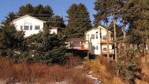 Une maison à deux étages dotée d’un balcon, entourée d’arbres denses et recouverte de neige.