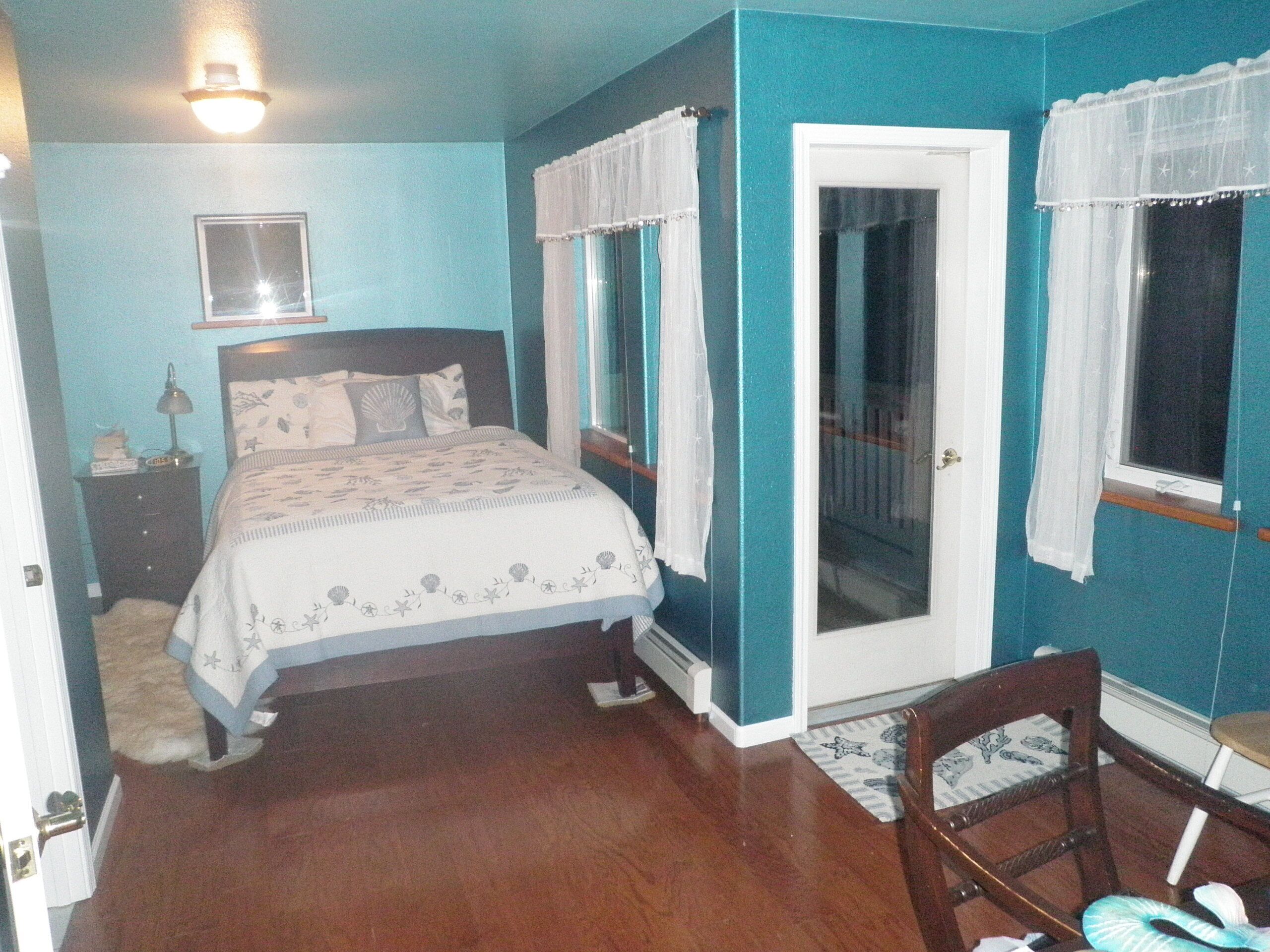 Un dormitorio con cama, mesita de noche, silla y puerta que da a otra habitación.