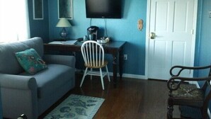 Un salon comprenant un canapé, un bureau avec une chaise, un téléviseur et une porte.