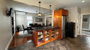 Eine moderne Küche mit einer zentralen Kochinsel, Holzschränken, einem Edelstahlkühlschrank und einem Essbereich mit Stühlen und Tisch.