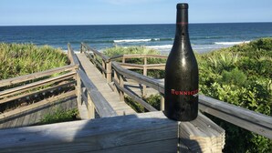Une promenade en bois menant à l’océan, avec une bouteille de vin Hunnicutt posée sur une rambarde.