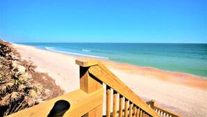 Un escalier en bois menant à une plage, avec un ciel dégagé.