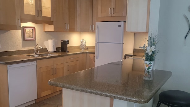 Una cocina con alacenas de madera, un refrigerador blanco, una encimera y dos taburetes.