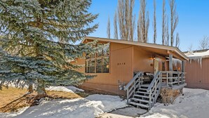 A wooden building with a staircase leading to a covered porch, surrounded by snow and bare trees. - Country Club Bungalow, Sleeps 4 (Flagstaff)
