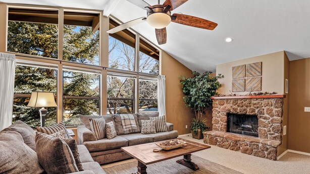 A spacious living room with a stone fireplace, large windows, and a ceiling fan. - Country Club Bungalow, Sleeps 4 (Flagstaff)