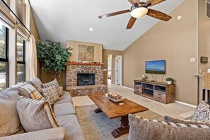 A living room with a stone fireplace, a ceiling fan, and a television. - Country Club Bungalow, Sleeps 4 (Flagstaff)