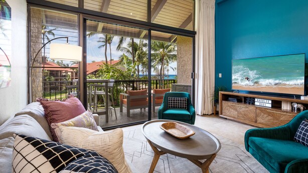 A living room with a large TV, comfortable seating, and a view of the ocean.
