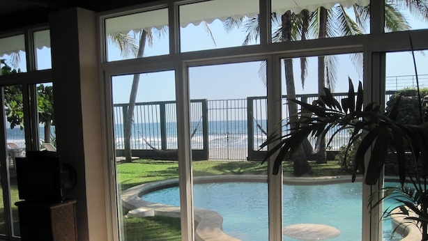 Ein Zimmer mit einer großen Schiebetür, die zu einem Poolbereich mit Blick auf das Meer und einen eingezäunten Strand führt.