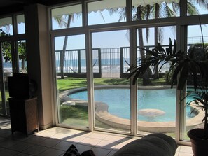 Ein Zimmer mit einer großen Schiebetür, die zu einem Poolbereich mit Blick auf das Meer und einen eingezäunten Strand führt.