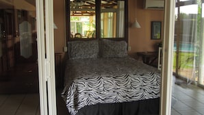 Ein Schlafzimmer mit einer zedernmuster-Bettdecke, einem Deckenventilator und Blick ins Freie durch eine Schiebetür.