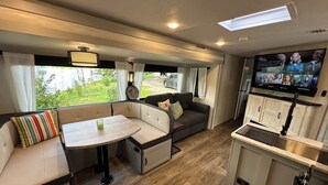 Een compact RV-interieur met een kitchenette, een eethoek en een zithoek met een televisie.
