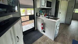 Een compacte keuken met een ingebouwde magnetron, een spoelbak en een kookplaat. Er is een klein raam met uitzicht op de omgeving.