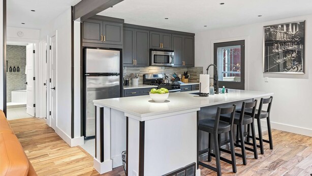 A modern kitchen with dark cabinets, stainless steel appliances, a central island with bar stools, and a large window. - Newly renovated 2BR Downtown, Main St, PCMR (Park City)