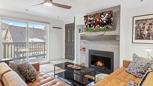 A modern living room with a fireplace, leather sofas, a glass coffee table, and a large TV mounted above the fireplace. - Newly renovated 2BR Downtown, Main St, PCMR (Park City)