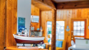 A model ship on a wooden stand in a room with wooden walls and windows. - BP:~Walk2Beach/Cafe/Golf/Store&Pub~Hottub~Bikes~Firepit~PingPong~Fenced~Dog (Seaside)
