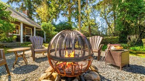 A fire pit with chairs and a table in a garden setting. - BP:~Walk2Beach/Cafe/Golf/Store&Pub~Hottub~Bikes~Firepit~PingPong~Fenced~Dog (Seaside)