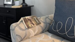 A sofa with a patterned fabric, a dark pillow with stitched text, a lamp, and a small plant on a side table. - Cozy updated 3 BR home steps away from downtown, space to relax and enjoy.  (Holland)