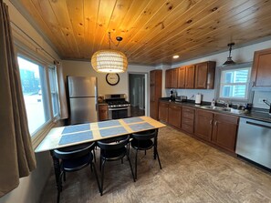 Una cocina moderna con armarios de madera, un refrigerador de acero inoxidable, una mesa de comedor con sillas y un ventanal grande.