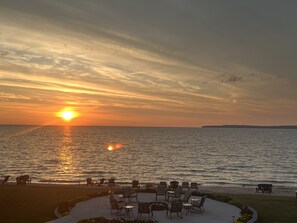 Solnedgang over et roligt hav med udendørs siddepladser og en græsplæne.