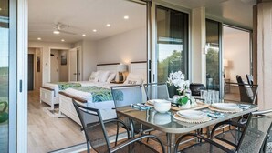 A modern bedroom with a bed, bedside table, and a view through a glass door. - Spacious 1BD w Exclusive Beach Cabana - Maui Eldorado K104 (Lahaina)