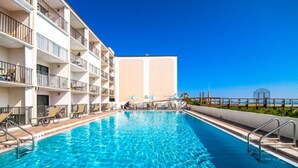 A swimming pool with sun loungers and a building with balconies in the background. - Direct Oceanfront Condo and Drive on the beach access!! (Saint Augustine)