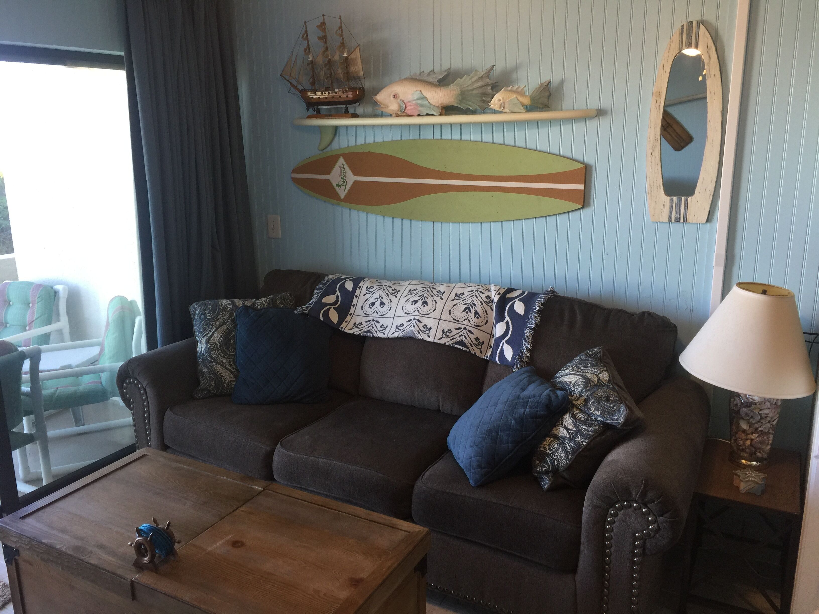 Un salon chaleureux avec un canapé marron, des coussins à motifs, une table basse en bois et une maquette de bateau posée sur une étagère.