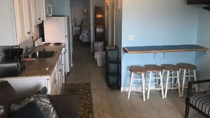 A compact kitchen with a central island, a dining area with stools, and a hallway leading to a bedroom. - Direct Oceanfront Condo and Drive on the beach access!! (Saint Augustine)