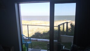 A living room with a wooden coffee table, a sofa, and a view of a beach through a glass door. - Direct Oceanfront Condo and Drive on the beach access!! (Saint Augustine)