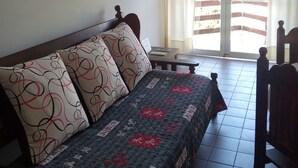 A room with a sofa, a table, and a chair. There is a window with curtains, and a door leading outside. - Departamento Temporario (Villa Carlos Paz)