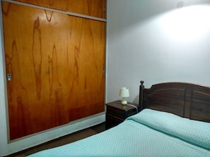 Une chambre à coucher avec une armoire en bois, une table de chevet avec une lampe et un lit recouvert d’une couvre-lit à motifs.