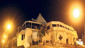 A building with a sign reading "Keops" at the top, surrounded by palm trees and a sloped landscape. - Departamento Temporario (Villa Carlos Paz)