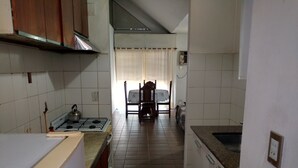 A kitchen with a gas stove, wooden cabinets, and a dining area with a table and chairs. - Departamento Temporario (Villa Carlos Paz)