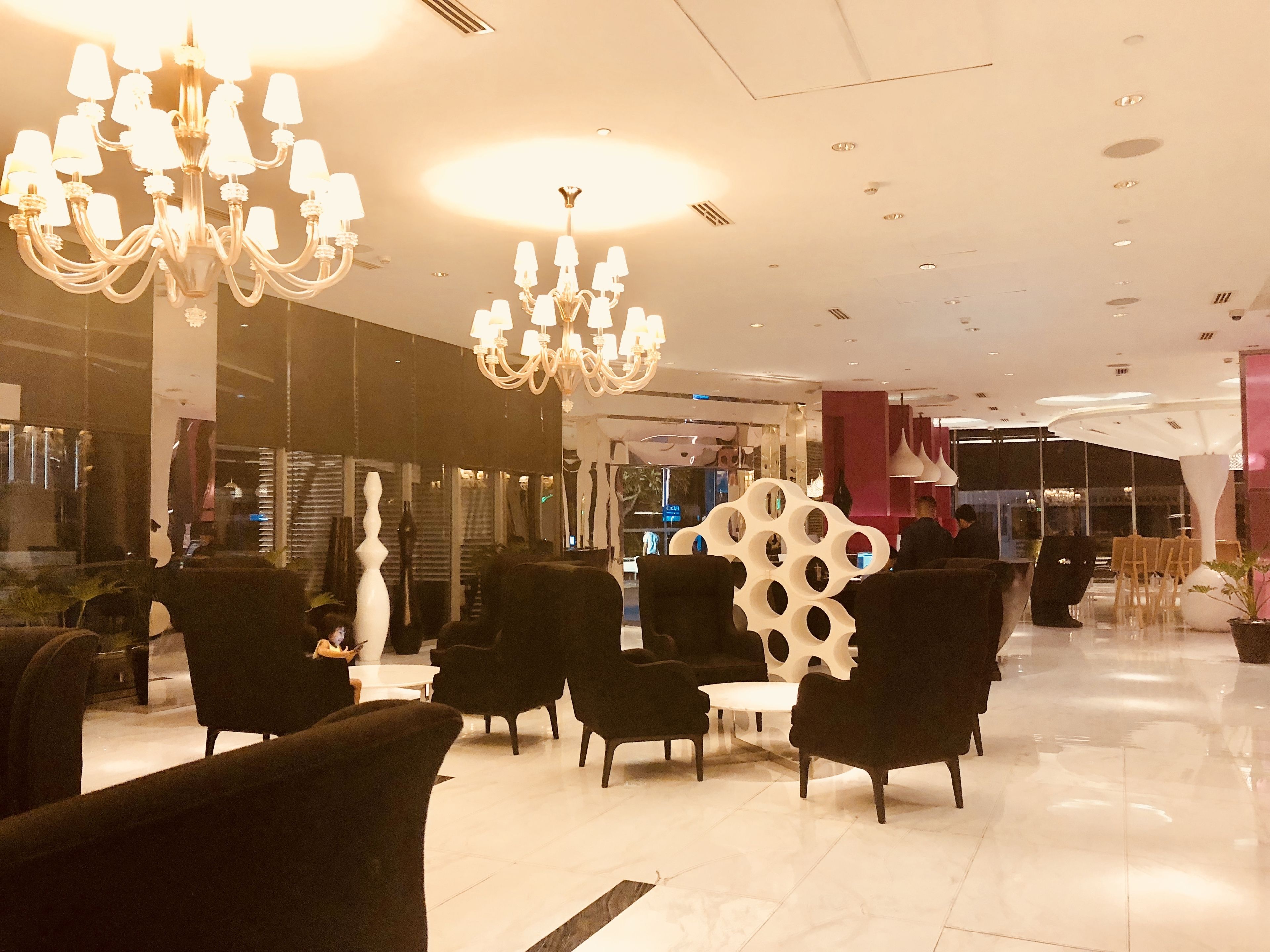 Eine moderne Lobby mit schwarzen Sesseln, einer weißen Wandgestaltung und Kronleuchtern.
