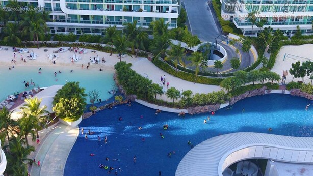A large outdoor swimming pool with multiple lanes, surrounded by palm trees and a modern building. - Azure Residences Condominium Daily Rental (Parañaque)