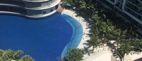 Un resort con una amplia piscina central, palmeras y un edificio circular con techo curvo.