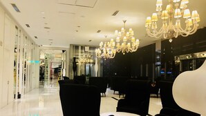A hotel lobby with black upholstered chairs, a white round table, and multiple chandeliers. - Azure Residences Condominium Daily Rental (Parañaque)