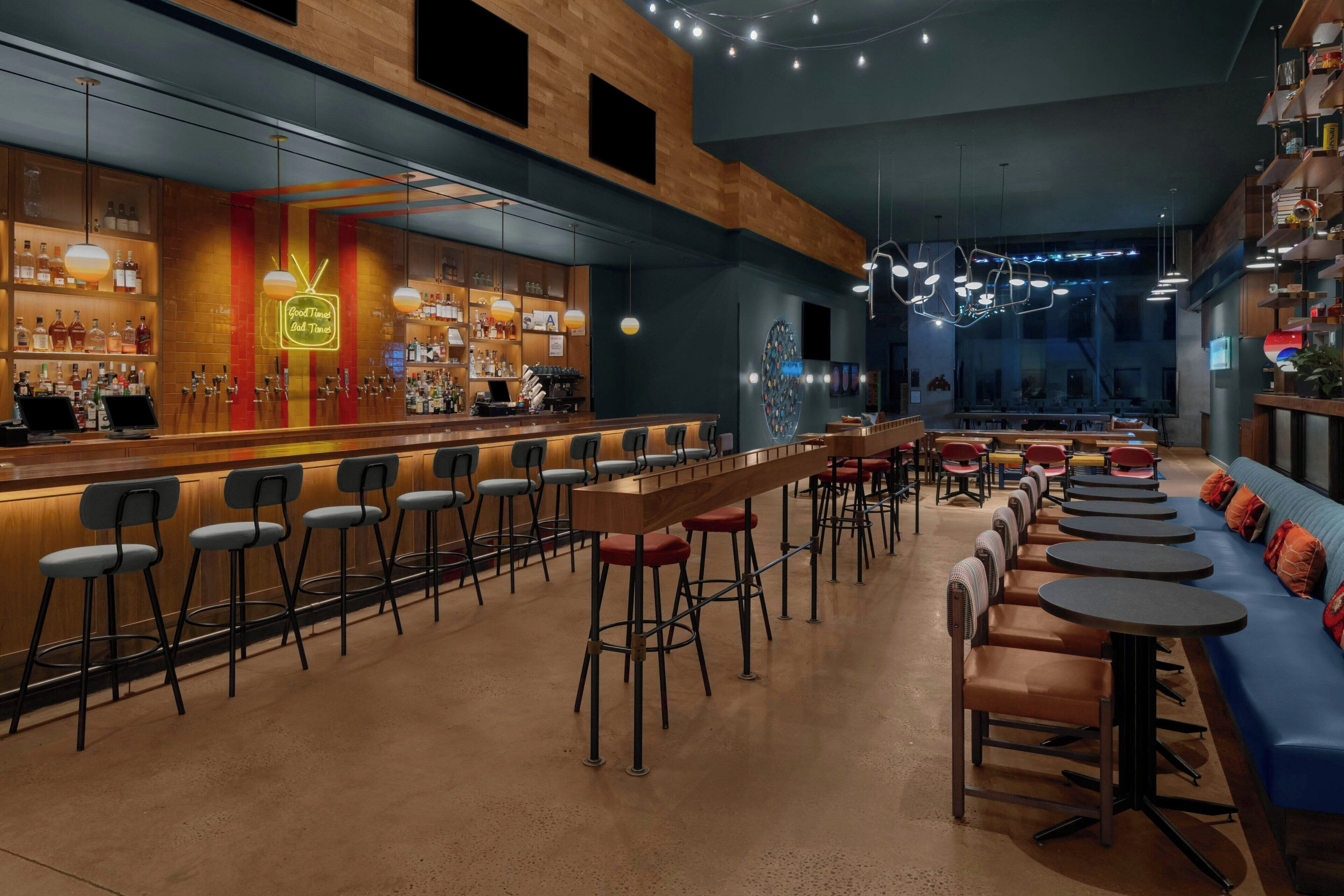 A modern bar area with a long counter, bar stools, and a seating area with round tables and chairs.