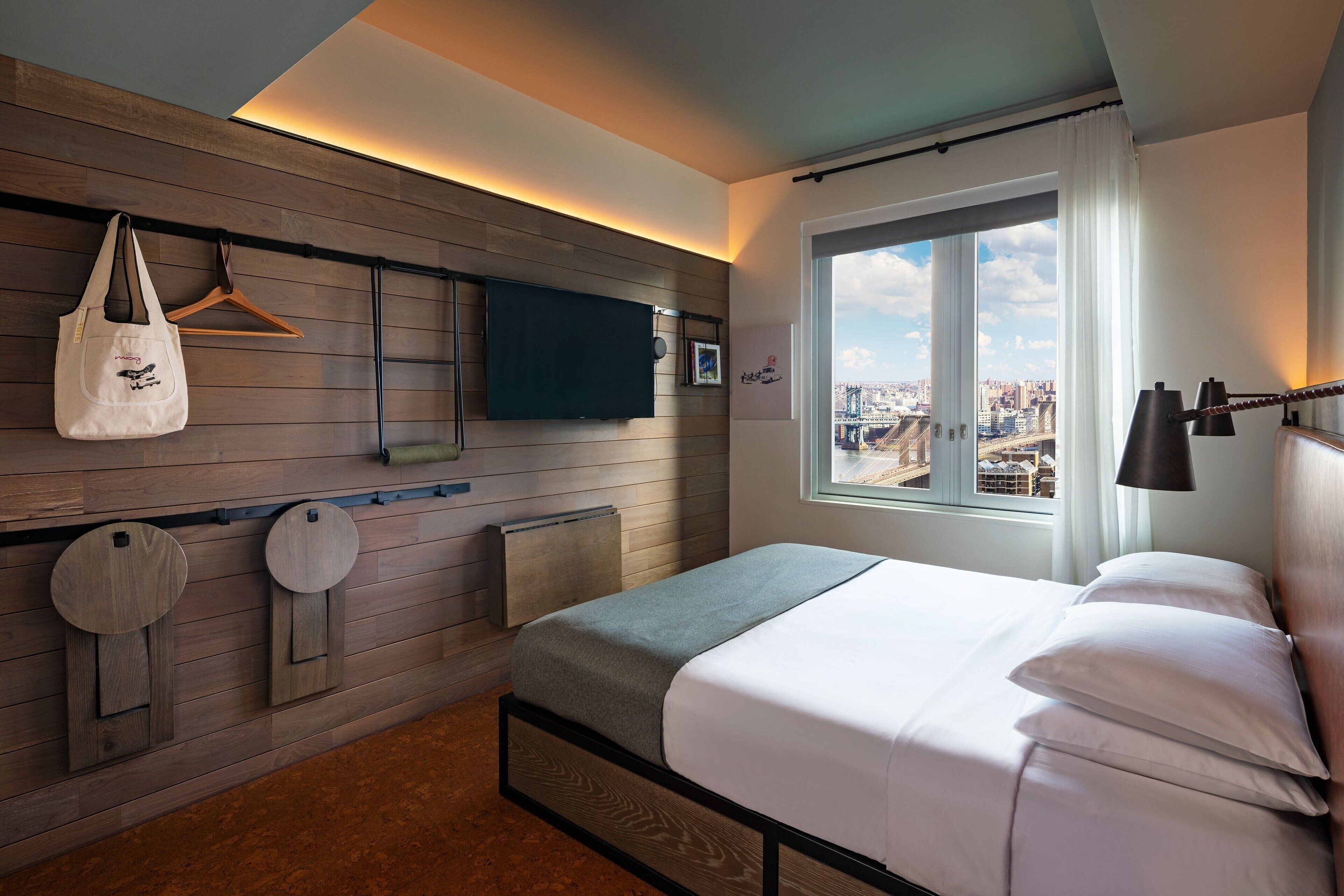 Habitación de hotel moderna con cama, televisor, vistas de la ciudad y un diseño de pared de madera.