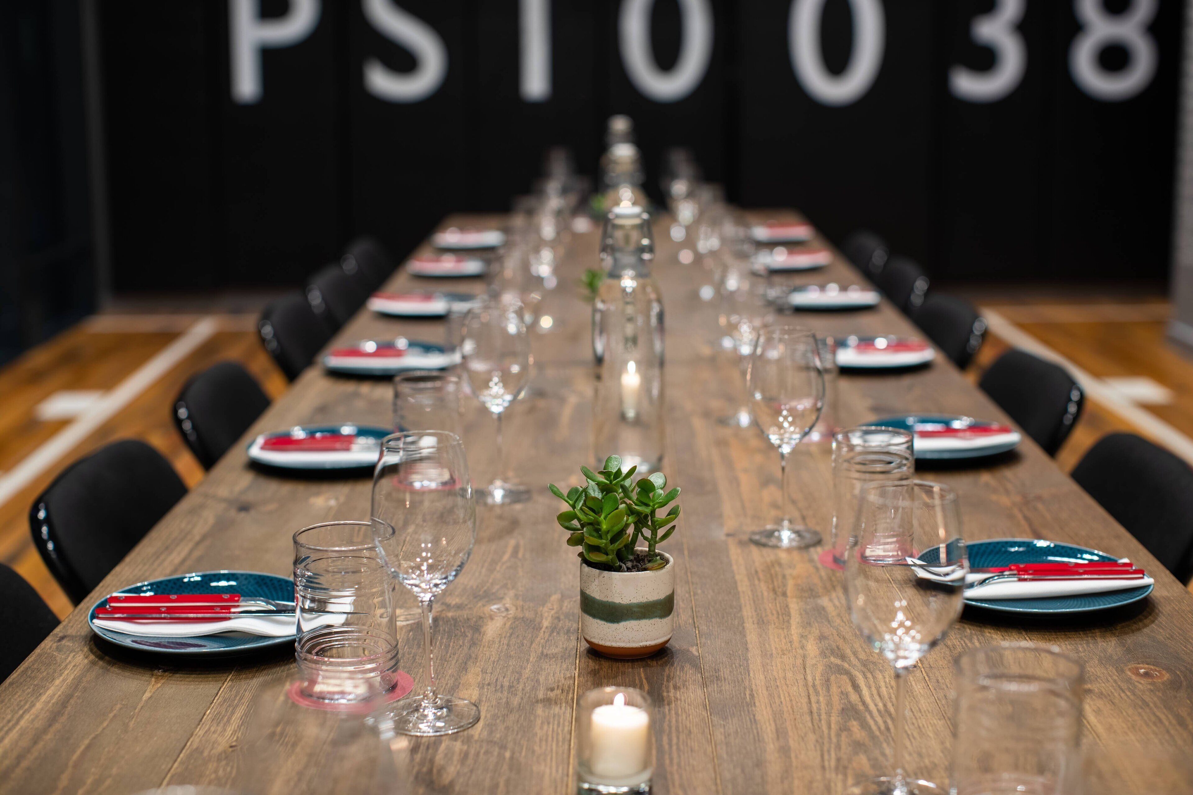 A long wooden table set for a meal with plates, glasses, and a small potted plant.