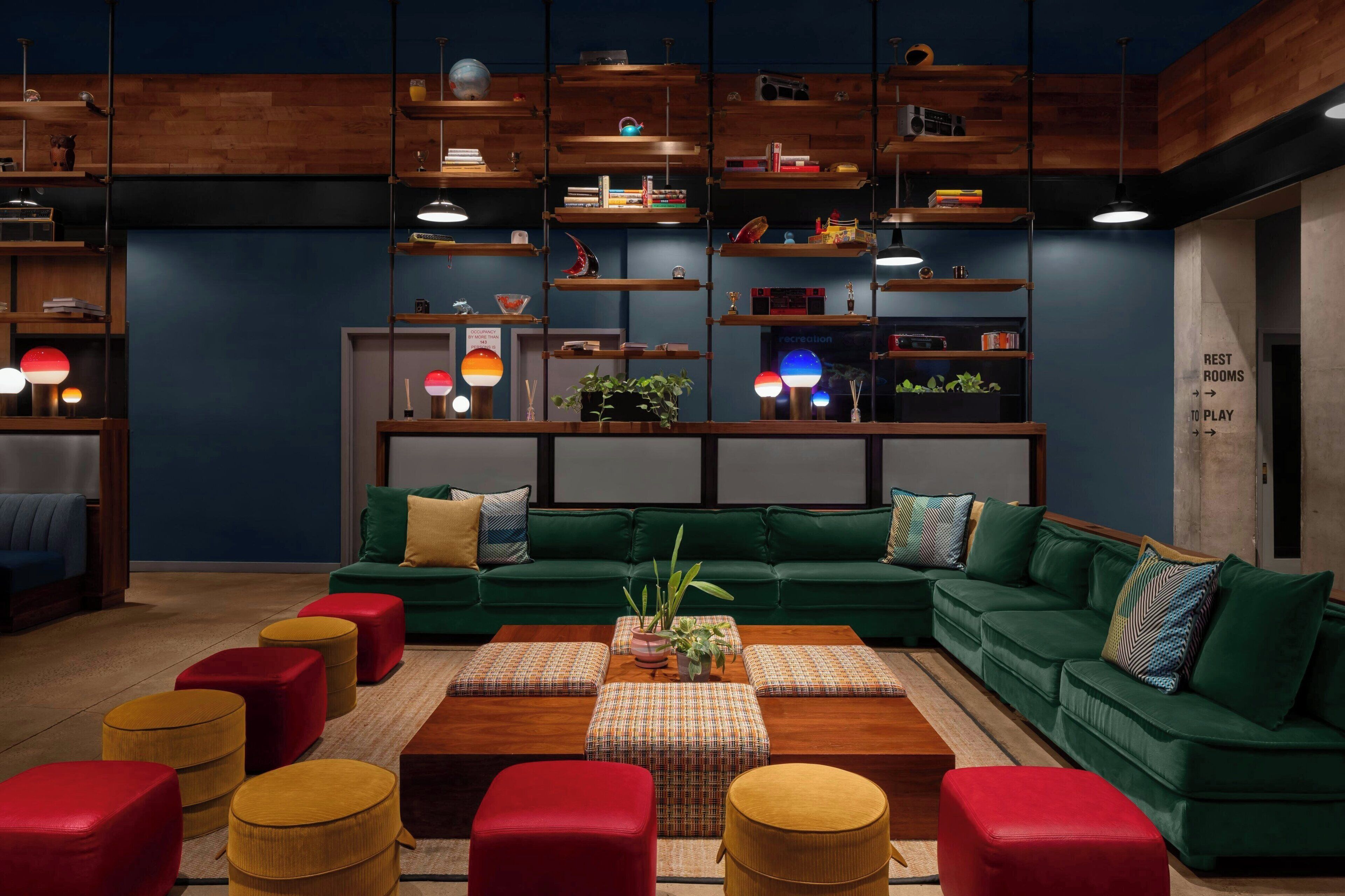 Una sala de estar moderna con un sofá seccional verde, otomanas rojas y amarillas, una mesa de centro de madera y estanterías con diversos objetos.