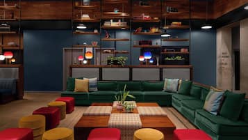 A modern living room with a green sectional sofa, red and yellow ottomans, wooden coffee table, and shelves with various items.