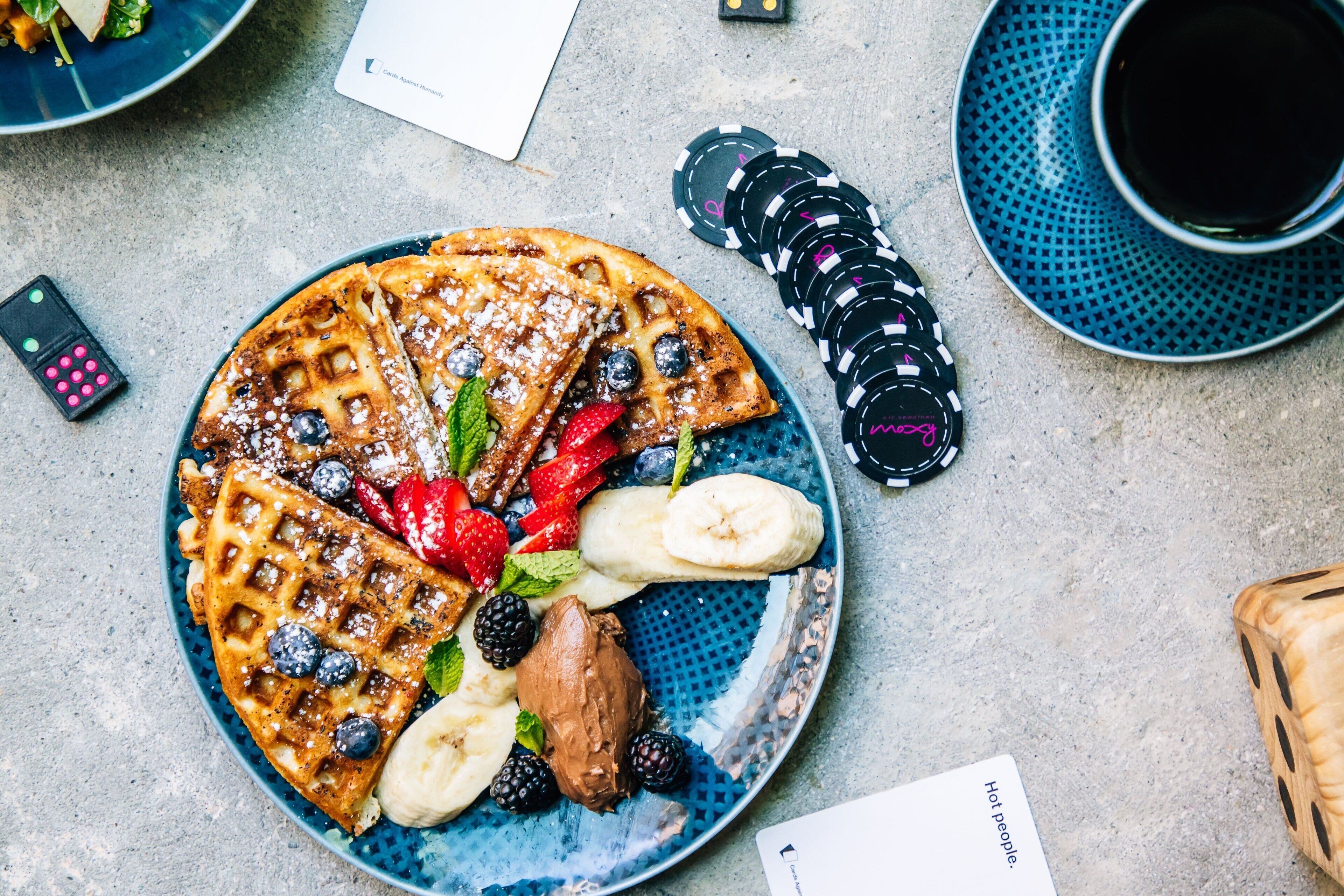 A plate of waffles with strawberries, blueberries, bananas, and chocolate sauce.