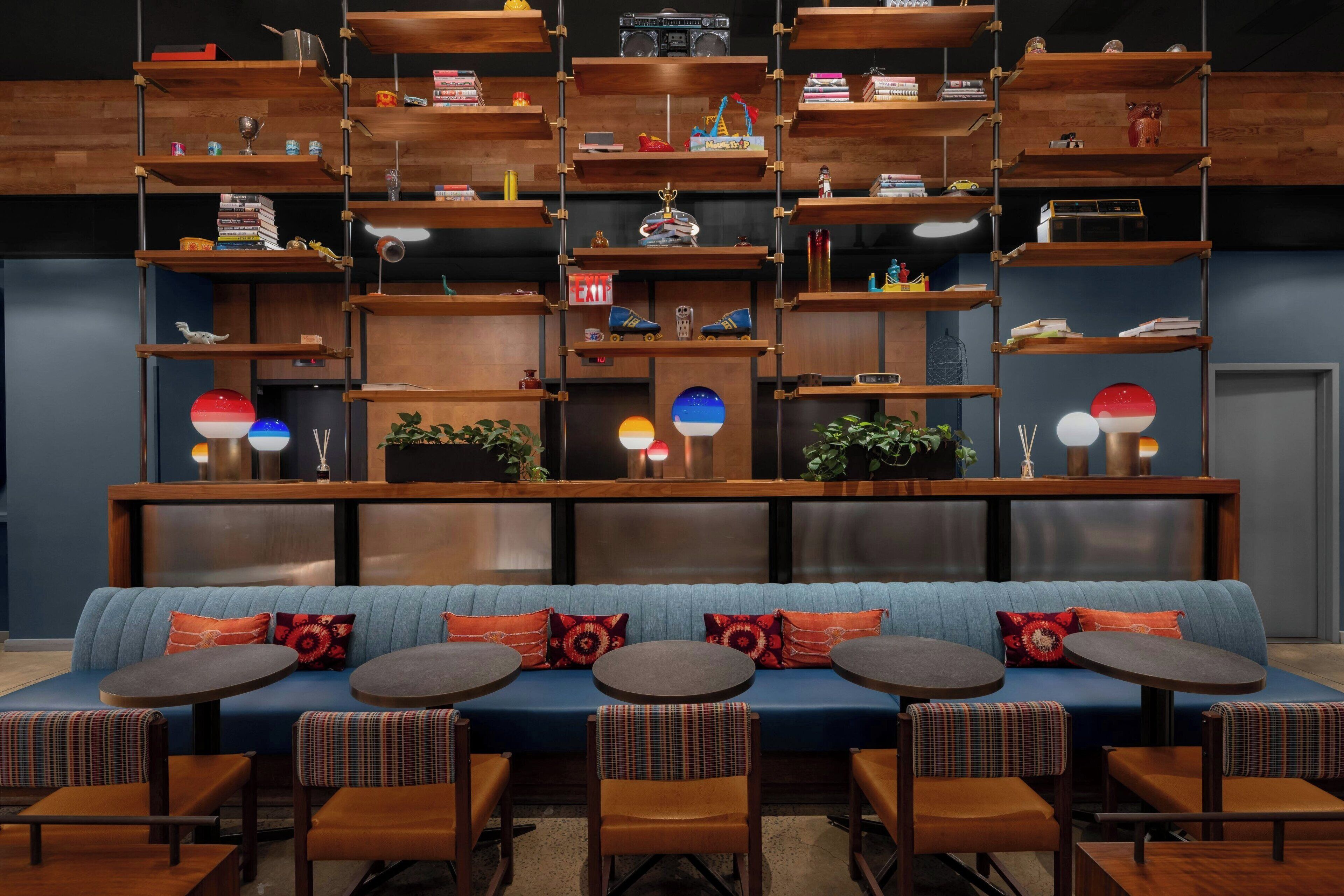 Un área de lounge moderna con un sofá azul, varias mesas redondas y una variedad de objetos en estantes de madera.