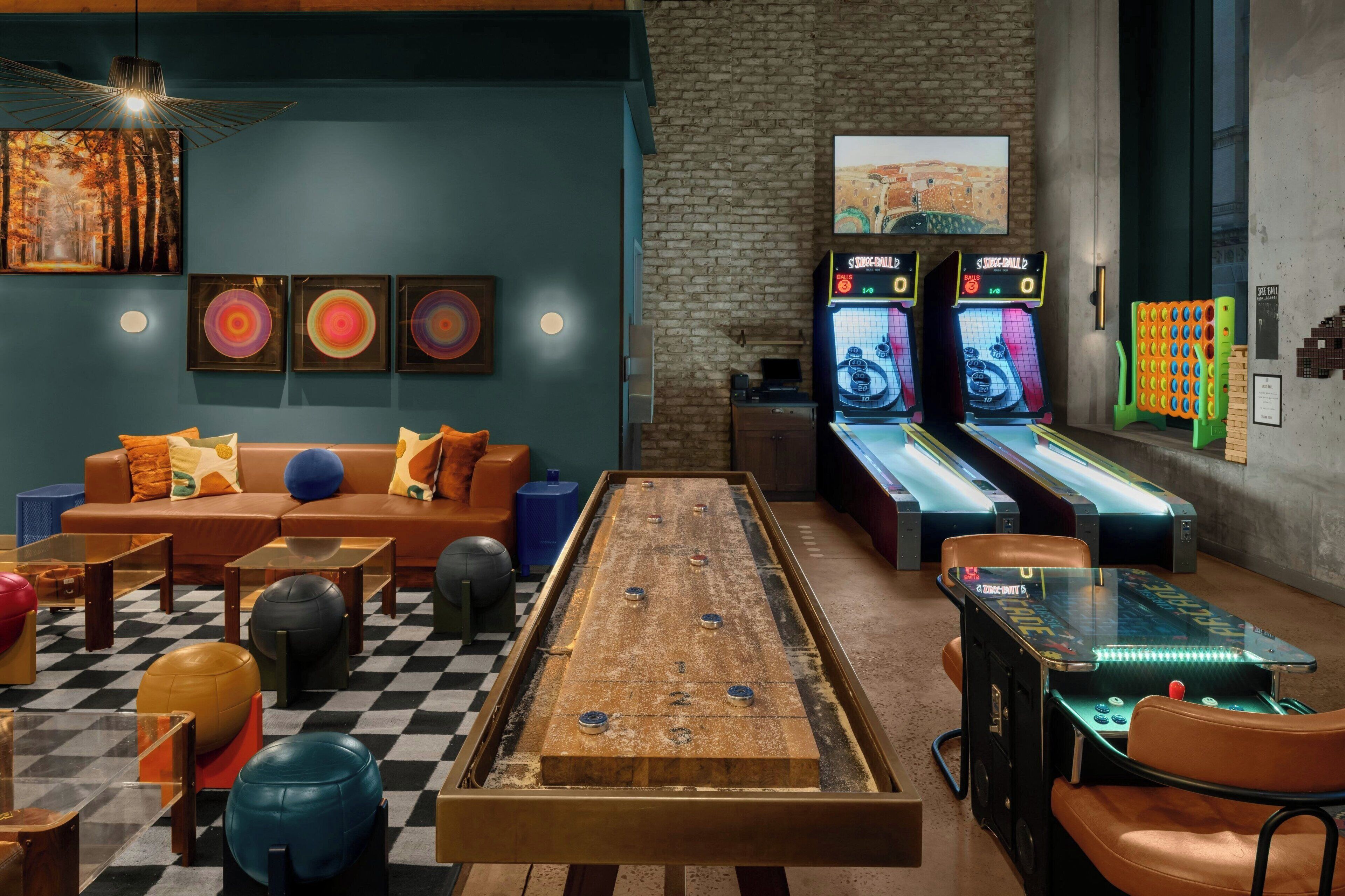 A room with a foosball table, two pinball machines, a billiards table, a sofa with cushions, and exercise balls.